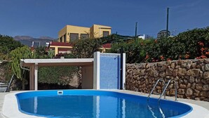 Une piscine entourée d’une terrasse en pierre, d’un mur en pierre et, au fond, d’un bâtiment à la façade jaune.
