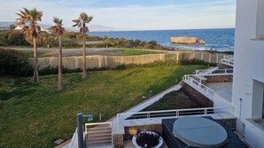A rooftop terrace with a view of the ocean, palm trees, and a white building. - Captivating 2-bed Apartment First Line Beach (Casares)