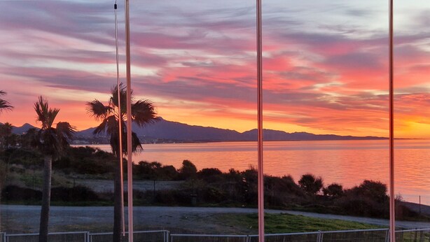 A sunset view with palm trees and mountains in the distance. - Captivating 2-bed Apartment First Line Beach (Casares)