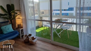 A modern living room with a large sliding glass door leading to an outdoor area with a green lawn and a white building in the background. - Apartment Fuengirola Carvajal Beachfront Malaga (Fuengirola)