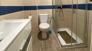 Ένα μπάνιο με μπανιέρα, τουαλέτα και ένα διαχωρισμένο χώρο ντους με γυάλινο διαχωριστικό.