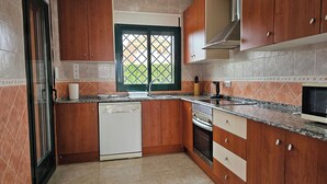A kitchen with wooden cabinets, a dishwasher, an oven, and a window with a view of greenery. - Private Pool- Rooftop Terrace & Bbq- Aircon (Zurgena)
