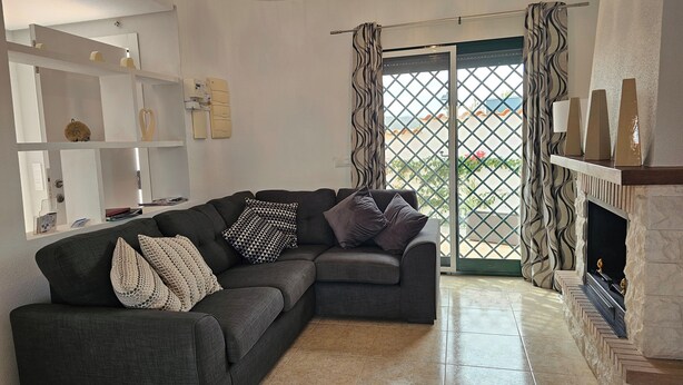 A living room with a dark grey sectional sofa, patterned pillows, a white shelving unit with decorative items, a fireplace, and a view through a patterned door. - Private Pool- Rooftop Terrace & Bbq- Aircon (Zurgena)