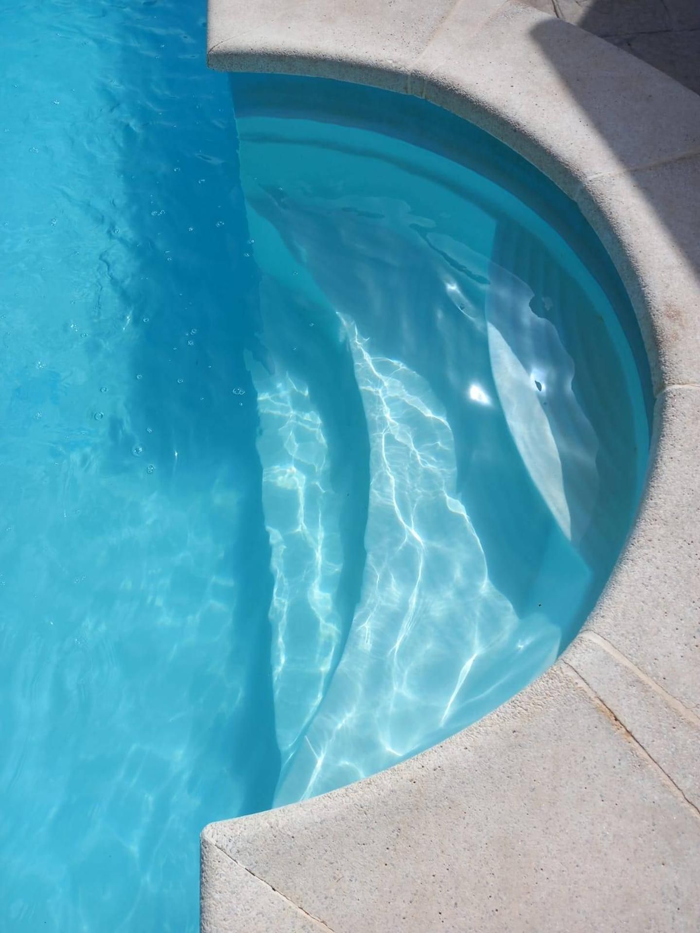 A clear blue swimming pool with a curved edge and a stone border.