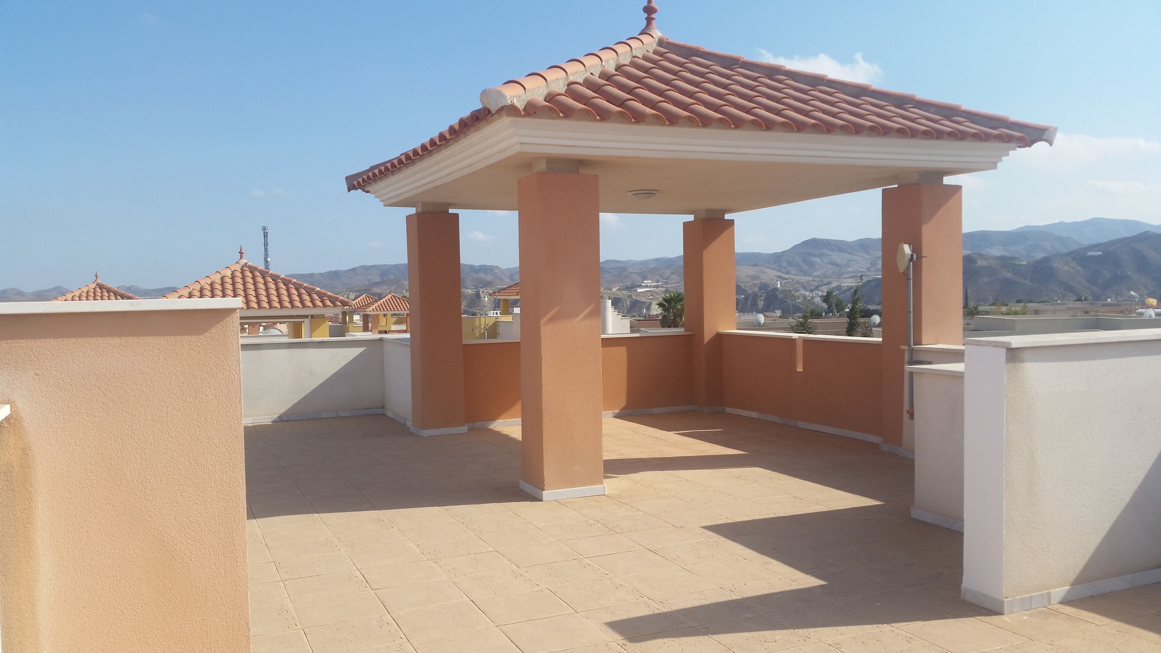 Une terrasse sur le toit dotée d’un espace salon couvert, d’un sol carrelé de couleur beige et offrant une vue sur les montagnes lointaines.