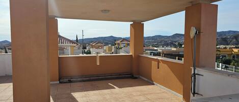 A covered outdoor balcony with a tiled floor, a ceiling fan, and a view of surrounding buildings and mountains.