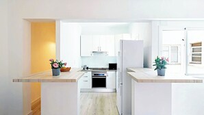 A modern kitchen with white cabinetry, a built-in oven, and a refrigerator. There are two potted plants on the countertops. - Light-flooded Loft in Santa Cruz (Santa Cruz de Tenerife)