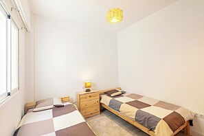 Ein kleines, sauberes Zimmer mit zwei Einzelbetten, einem Holzschrank, einer Nachttischlampe und einer Pendelleuchte.