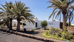 Un edificio blanco con palmeras y un muro de piedra al frente.