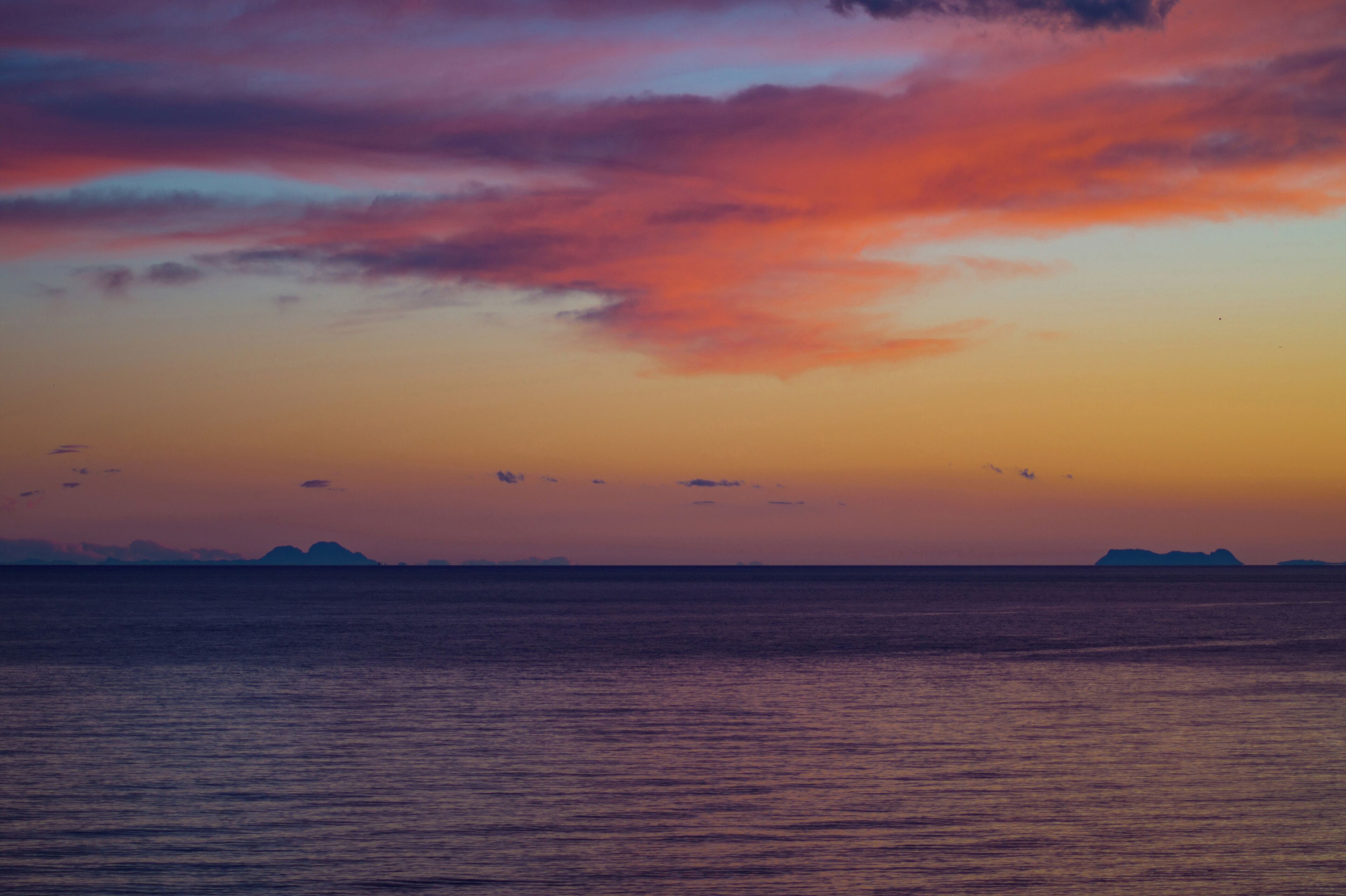 A sunset over a calm sea with distant landforms.