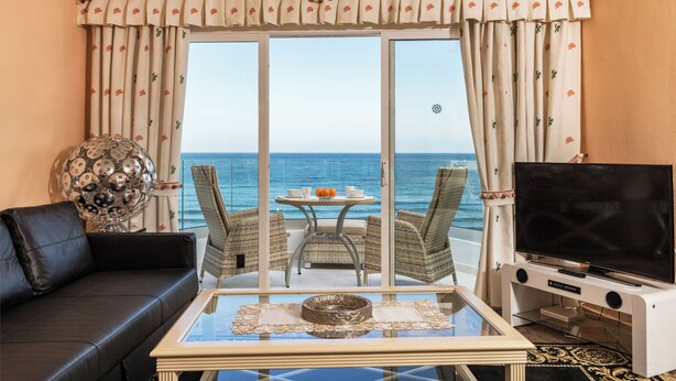 Ein Wohnzimmer mit einer Couch, einem Couchtisch, einem Fernseher und Meerblick.