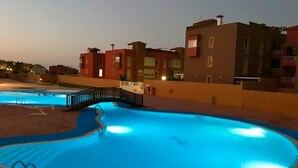 A swimming pool with a bridge, surrounded by buildings with balconies. - Relaxing and Welcoming Villa, Corralejo, Canaries (La Oliva)