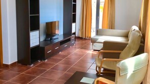 A spacious living room with a flat-screen TV, a sofa, and two armchairs. There are built-in shelves and a large window with curtains. - Relaxing and Welcoming Villa, Corralejo, Canaries (La Oliva)
