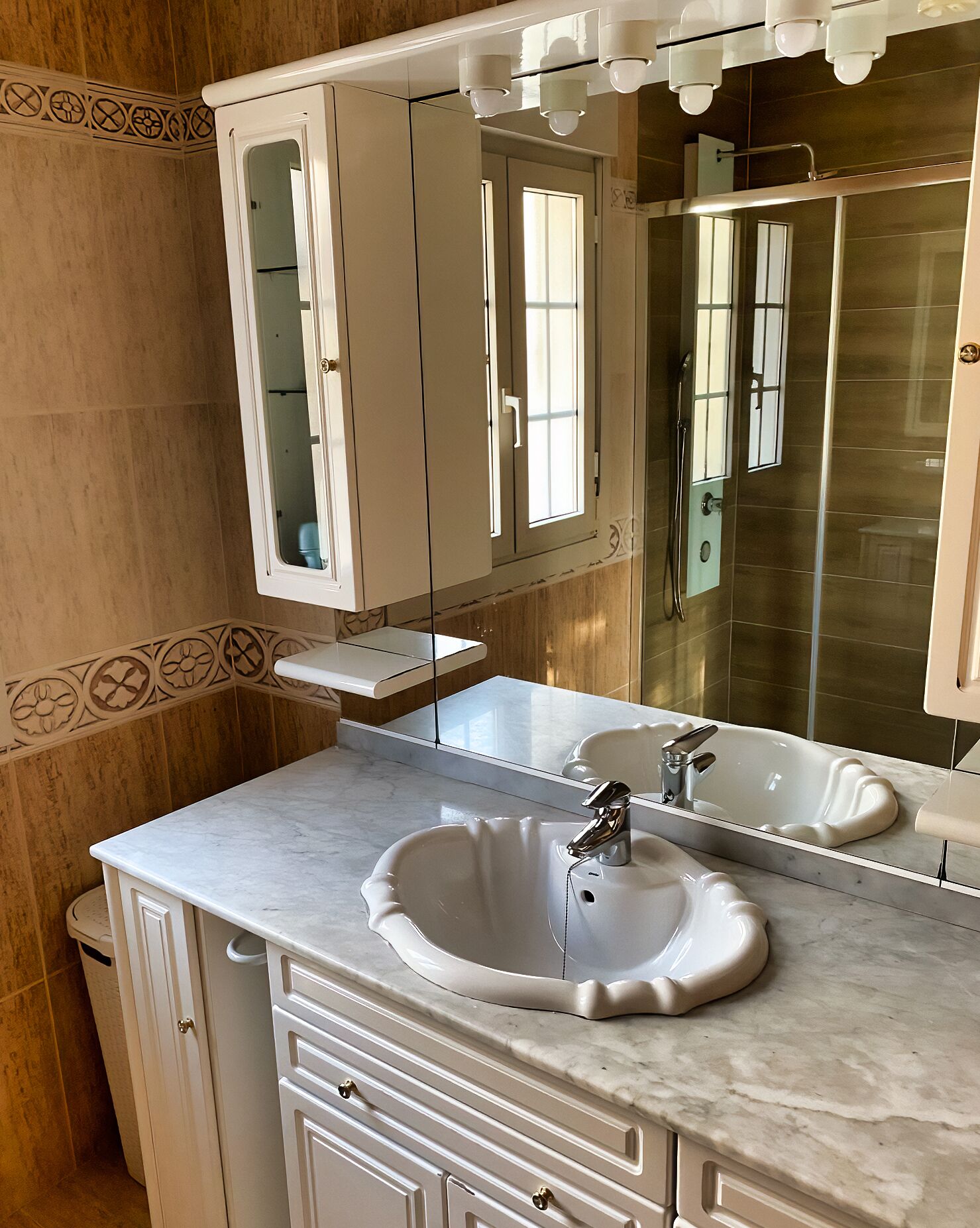 A bathroom with a white marble sink, a large mirror, and a cabinet with a decorative border.