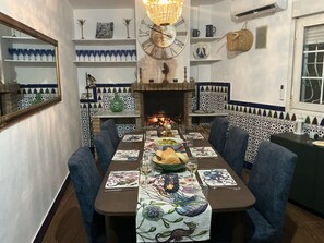 Ein Essbereich mit einem langen Tisch, der für eine Mahlzeit gedeckt ist, mit blauen Stühlen, einer Zieruhr und einem Kamin.