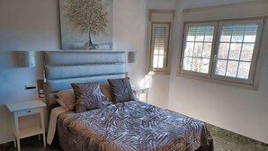 Een slaapkamer met een bed, nachtkastjes, een schilderij en een raam met jaloezieën.