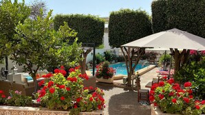 Een zwembadterras met een pergola, zitplaatsen en decoratieve planten.