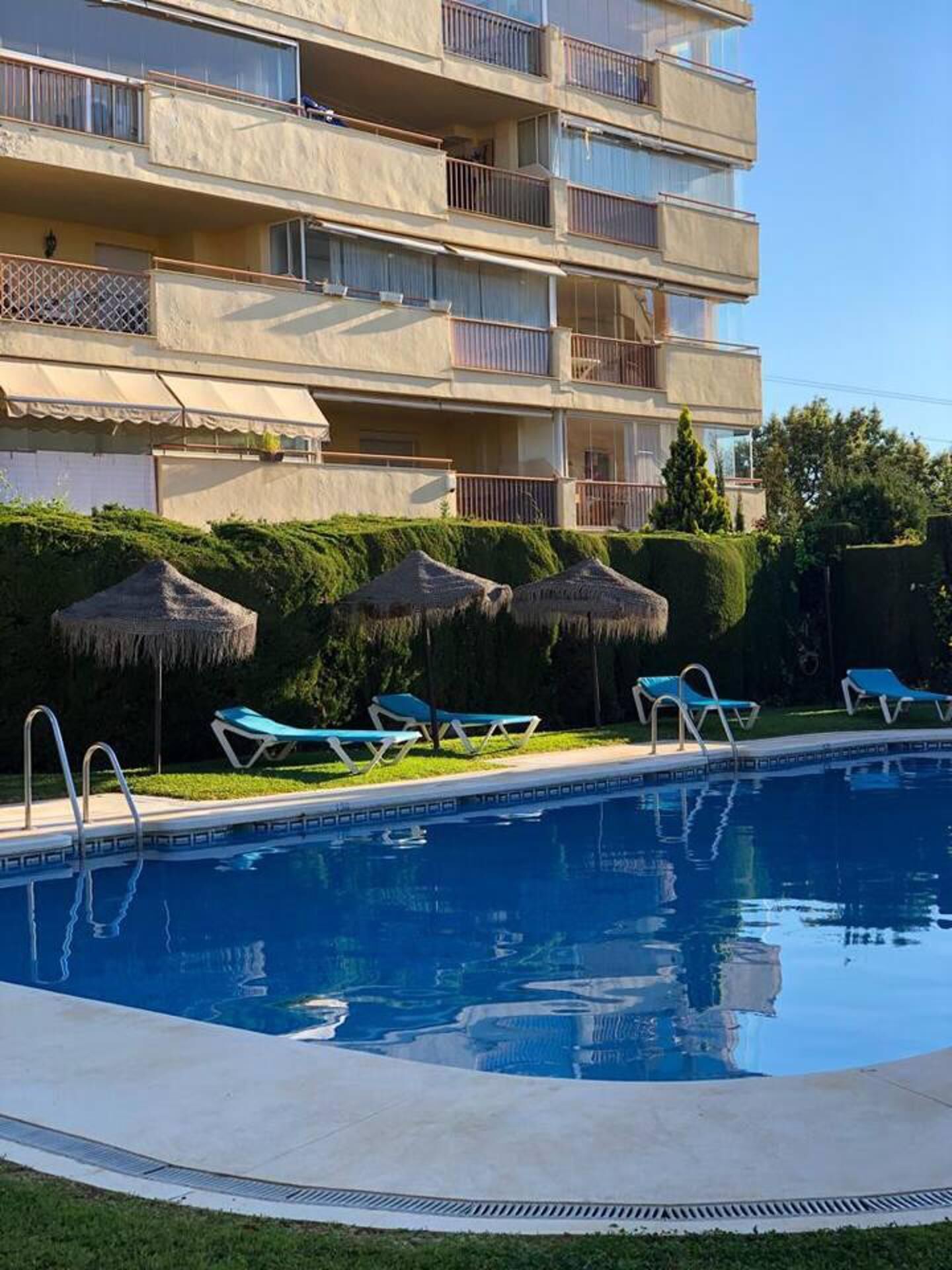 A swimming pool with lounge chairs and a building with multiple balconies in the background.