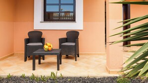 Eine Terrasse mit zwei Korbstühlen, einem Tisch mit Obst und einem Fenster mit Blick.