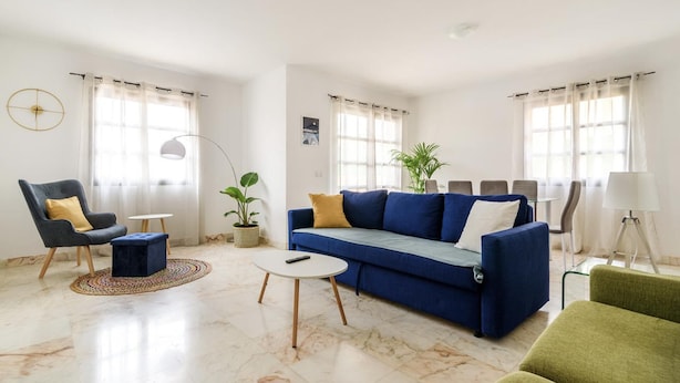 Ein modernes Wohnzimmer mit einem blauen Sofa, einem grünen Sessel, einem runden Couchtisch und einer Stehlampe.