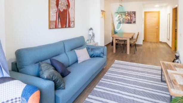A living room with a blue sofa, a dining table with chairs, and artwork on the walls. - 3 Bed Apartment Sleeps 6 - Free Parking & Balcony (Estepona)