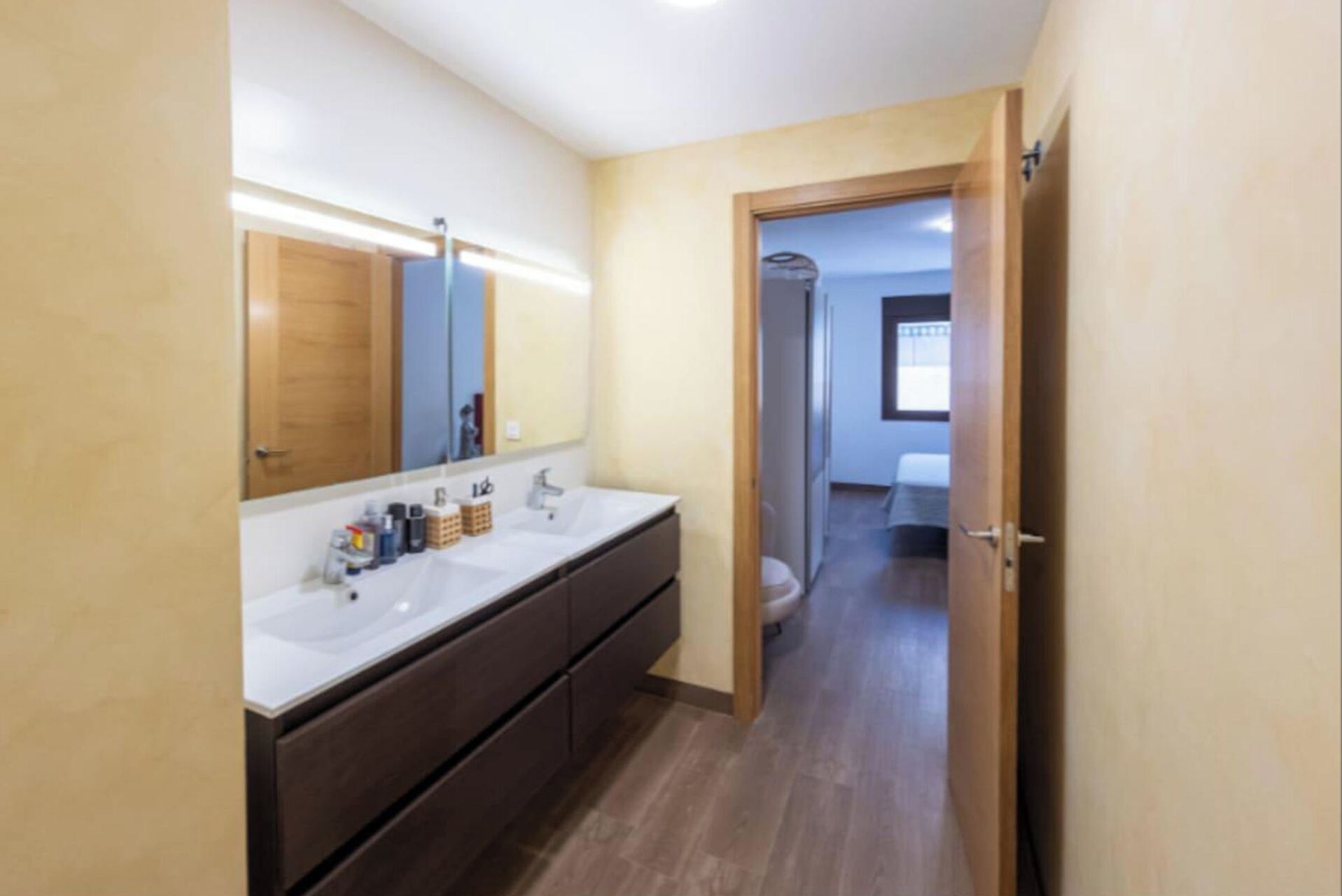 A modern bathroom with a large mirror, dual sinks, and a wooden floor.