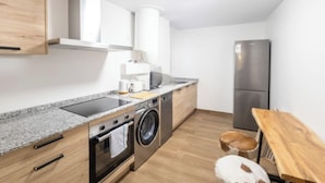 A compact kitchen with a washing machine, a refrigerator, and a wooden table. - 3 Bed Apartment Sleeps 6 - Free Parking & Balcony (Estepona)