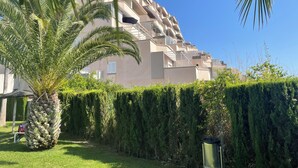 Un edificio moderno con balconi, circondato da siepi curate e una palma.