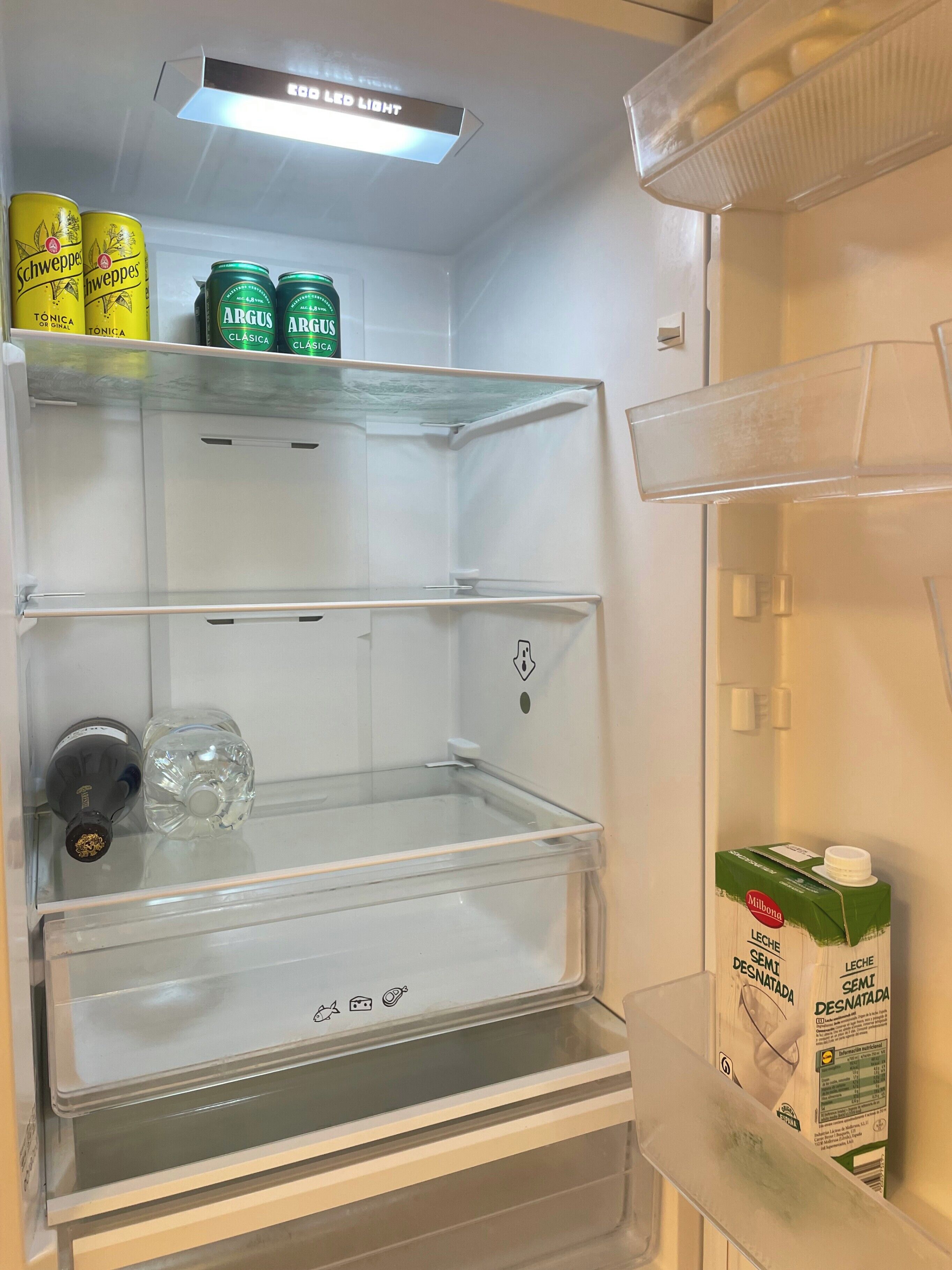 Un refrigerador con tres estantes, una caja de leche y dos botellas.