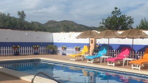 A swimming pool with a white fence, colorful lounge chairs, and potted plants.