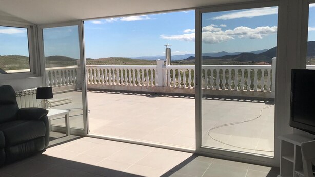A spacious balcony with a clear view of the landscape, a white railing, and a flat-screen TV on a stand.