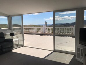 Een ruim balkon met vrij uitzicht over het landschap, een witte balustrade en een flatscreen televisie op een standaard.