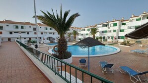 Area piscina con lettini, una palma e un edificio sullo sfondo con balconi.