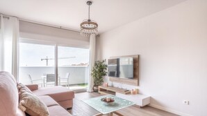 A modern living room with a sofa, a coffee table, a TV, and a balcony with a view of the city. - Stunning Apartment in Estepona, Spain Private Pool (Estepona)