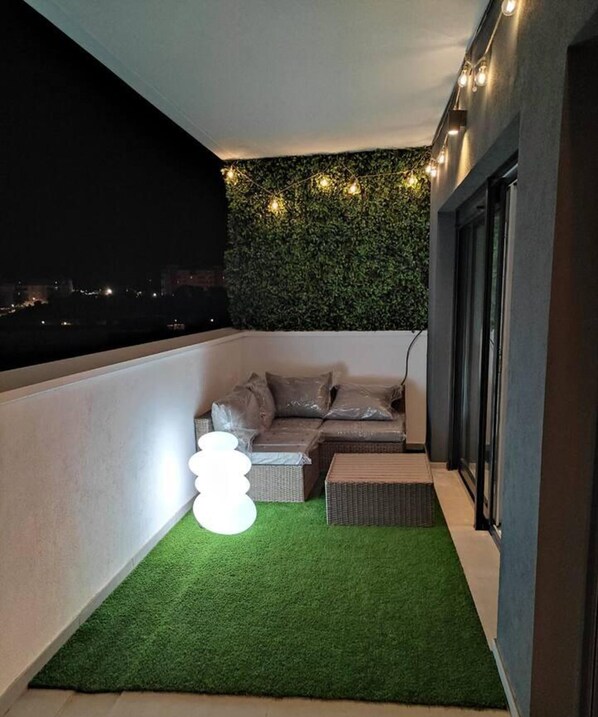 A balcony with a green artificial turf, a wicker sofa, and a white spherical light fixture.