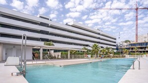 A modern building with a swimming pool, a covered area with stairs, and a construction crane in the background. - Stunning Apartment in Estepona, Spain Private Pool (Estepona)