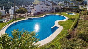 A swimming pool with a curved edge, surrounded by a fence and lush greenery. - Albatross Golf Suite Alcaidesa (San Roque)