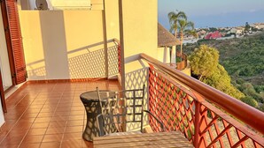 A balcony with a wooden table and chairs, a red railing, and a view of a hillside with houses. - Albatross Golf Suite Alcaidesa (San Roque)