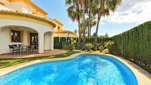 Une piscine dont le fond est décoré de motifs géométriques en mosaïque, entourée d’une pelouse bien entretenue et de palmiers.