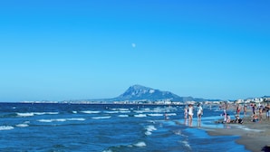 Une plage avec des vagues, des gens et une montagne en arrière-plan.