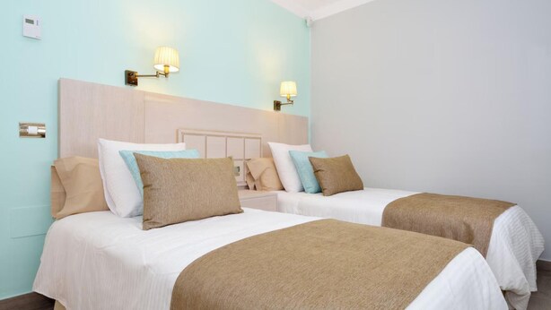 A hotel room with two beds, light blue walls, and wall-mounted lamps. - 3bed Villa- Pool, Outdoor Dining Terrace, Sea View (Tías)