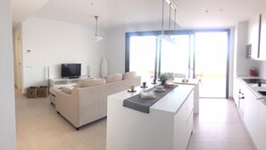 A modern living room with a sofa, a coffee table, and a TV. There is a kitchen area with a counter and cabinets. - Stunning Apartment Close to Golf, Mijas, Spain (Mijas)
