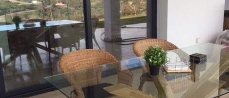 A dining area with wicker chairs and a glass table, overlooking a scenic landscape.