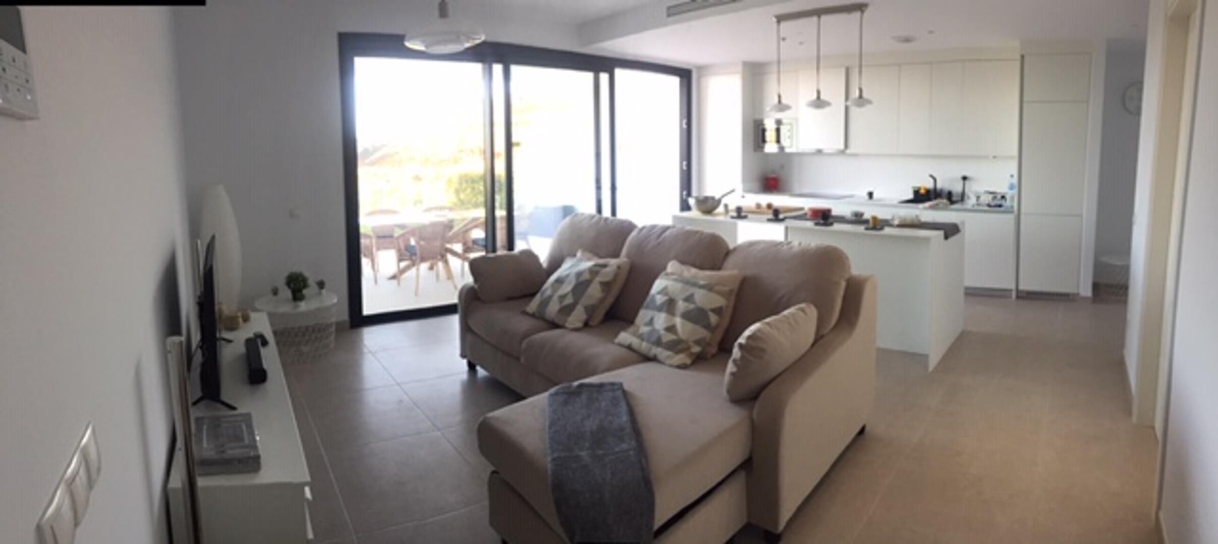 A modern living room with a sofa, a TV, and a sliding glass door leading to a balcony.