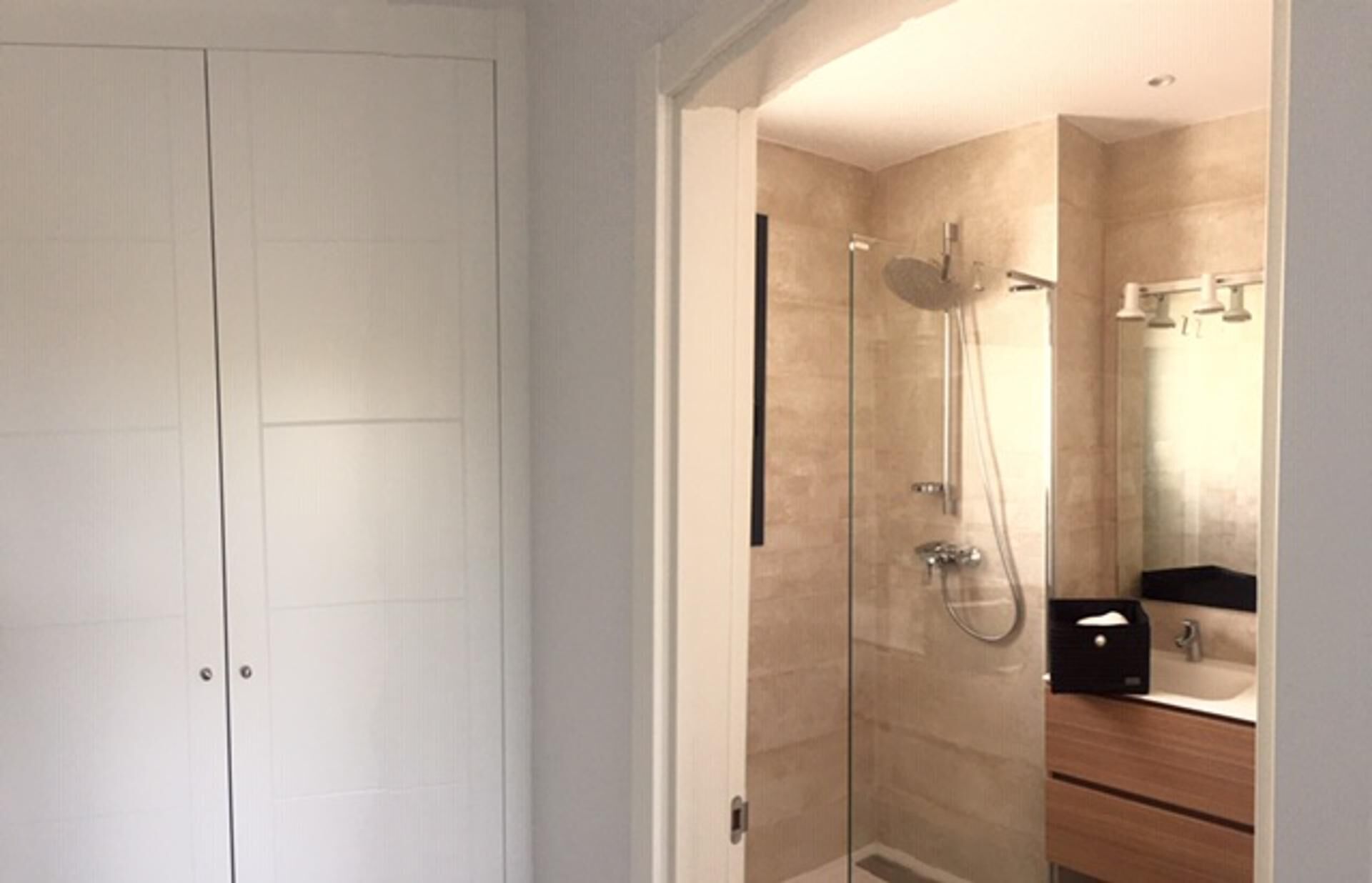 A modern bathroom with a glass-enclosed shower, a wooden vanity, and a mirror.