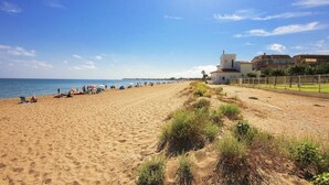 A sandy beach with people and umbrellas, a grassy area, and buildings in the background. - Apartam Tierra del Mediterraneo Next to the Beach (Denia)