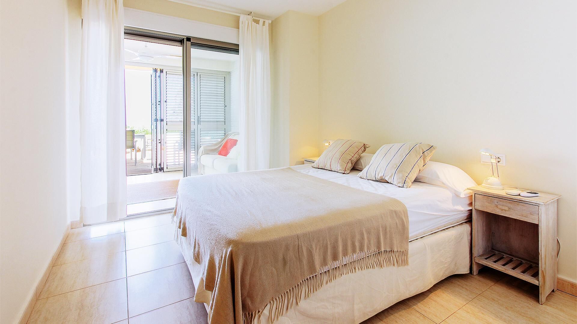 Un dormitorio con una cama, una mesita de noche, una lámpara y vistas a un balcón.