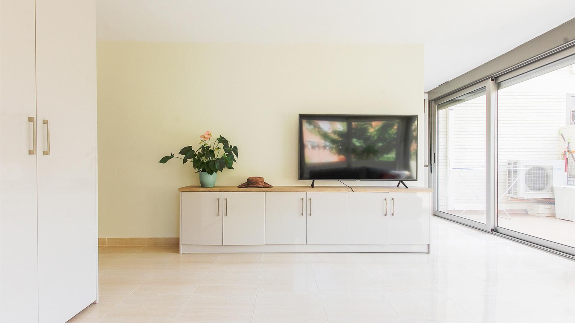 A modern living room with a flat-screen TV on a white cabinet, a potted plant, and a hat.