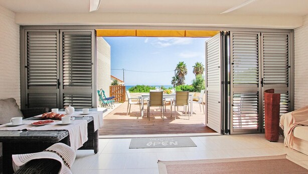 A room with a dining area, a sofa, and a view of the sea. - Apartam Tierra del Mediterraneo Next to the Beach (Denia)