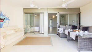 A modern living room with a sofa, a wicker table set for dining, and a sliding glass door leading to a bedroom. - Apartam Tierra del Mediterraneo Next to the Beach (Denia)
